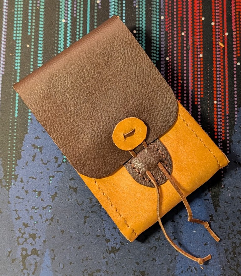 a belt pouch made of brown and tan leathers, with a leather lace closure wrapping around a leather button