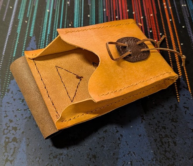 a belt pouch made of brown and tan leathers, the flap is open to reveal the raw flesh-side interior of the leather panels