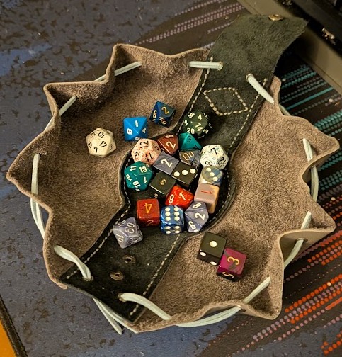 a drawstring pouch made of gray and black leathers, spread out into a circle with the edge curled up to keep dice from rolling out