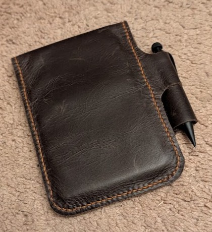 a dark brown leather notepad cover, with a black mechanical pencil hanging through a pen loop on one side